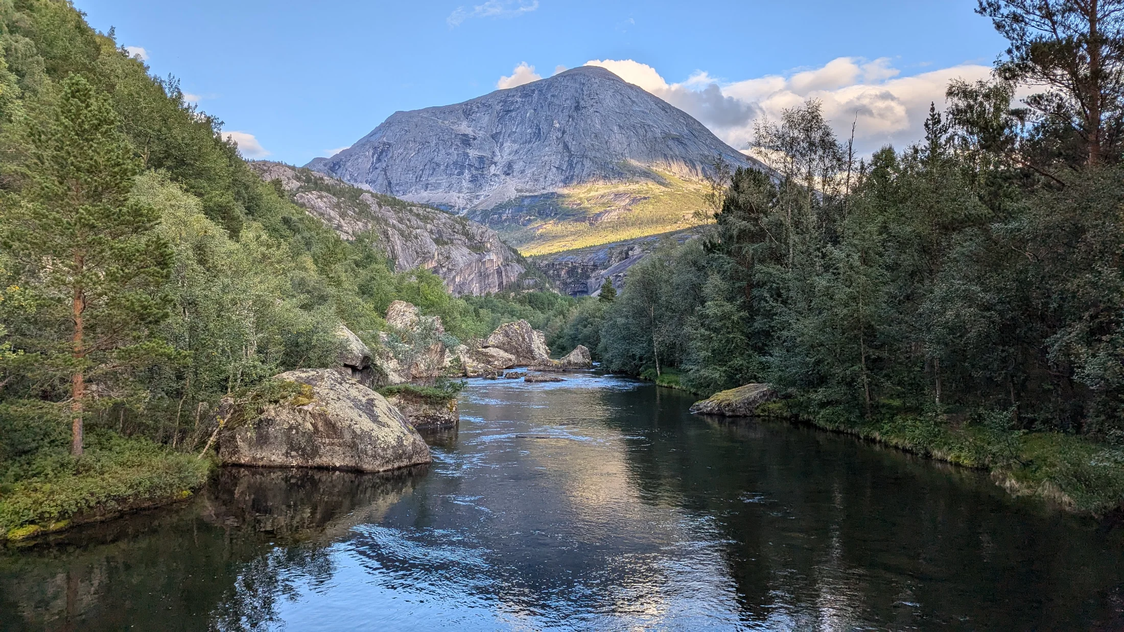 Forested mountain river beneath a rocky peak.